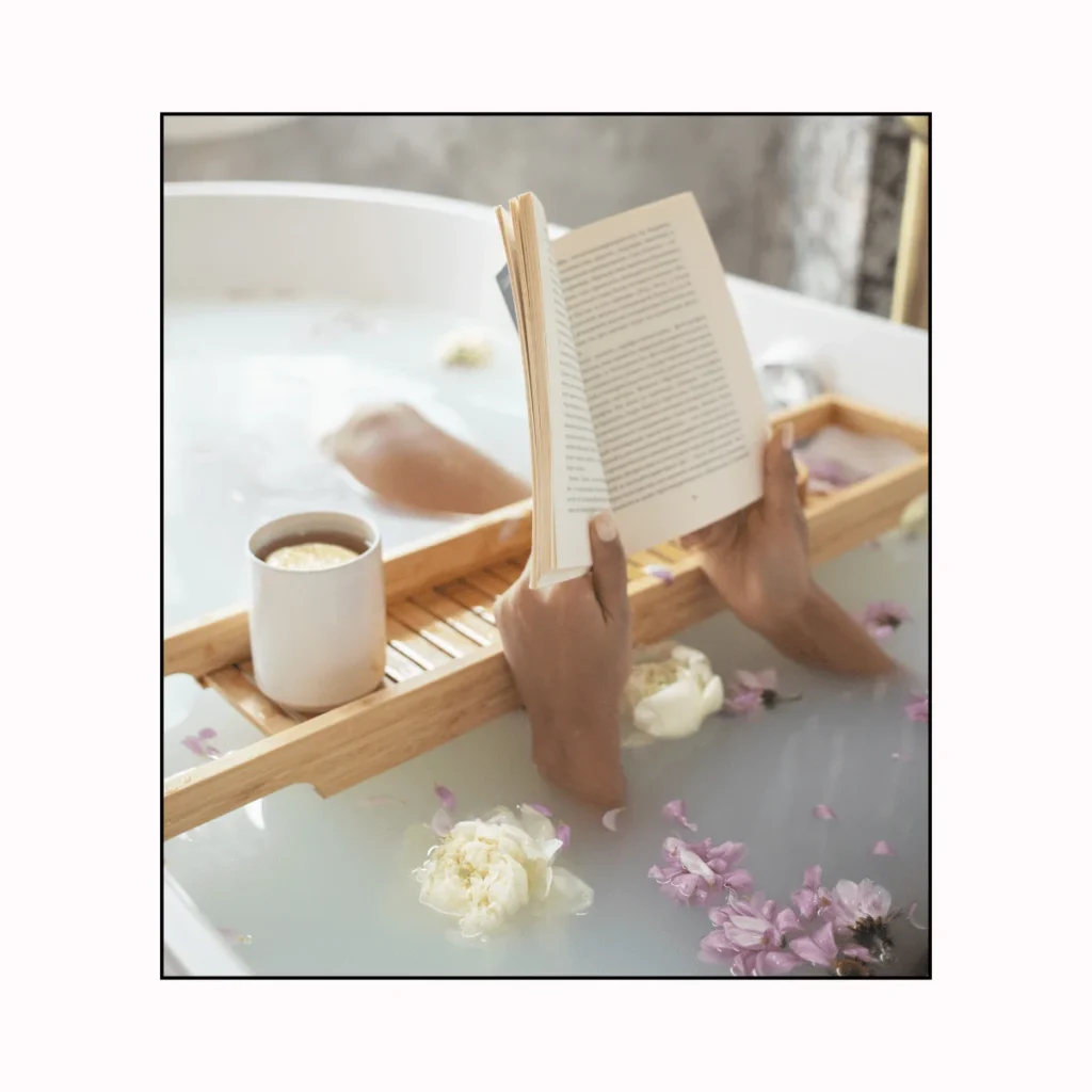 A woman having a bath flower petals reads a book. fun ideas for self-care Sundays