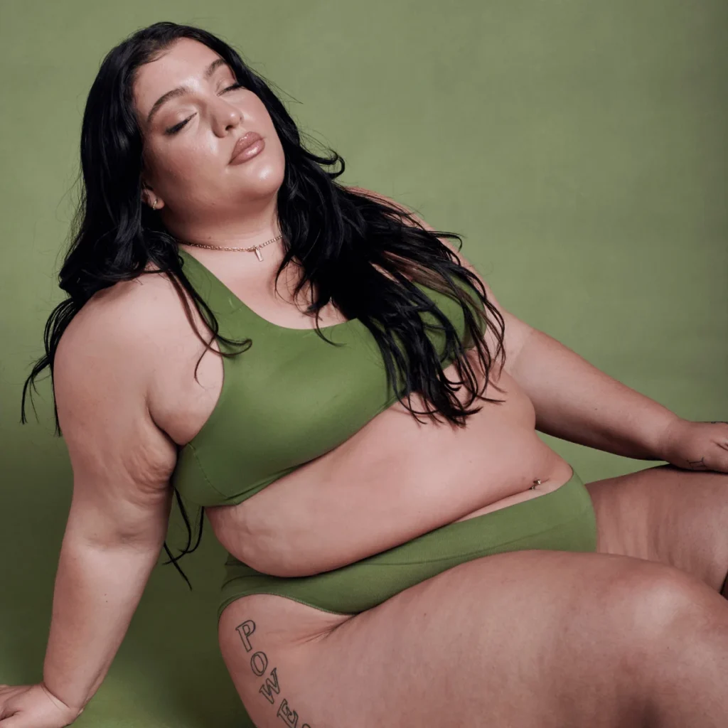 A woman poses with her eyes closed wearing green athletic undergarments