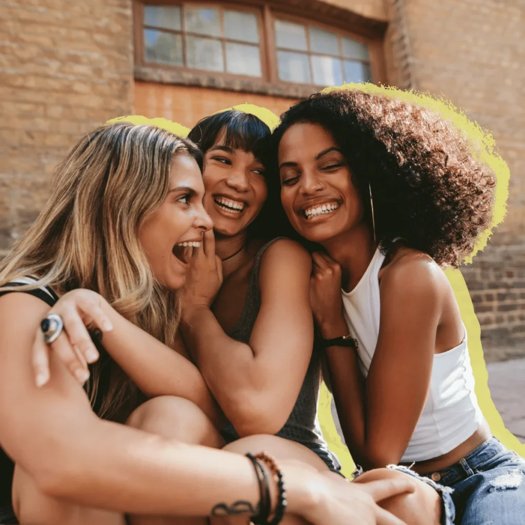 Three young female friends laughing while sitting down outside a building