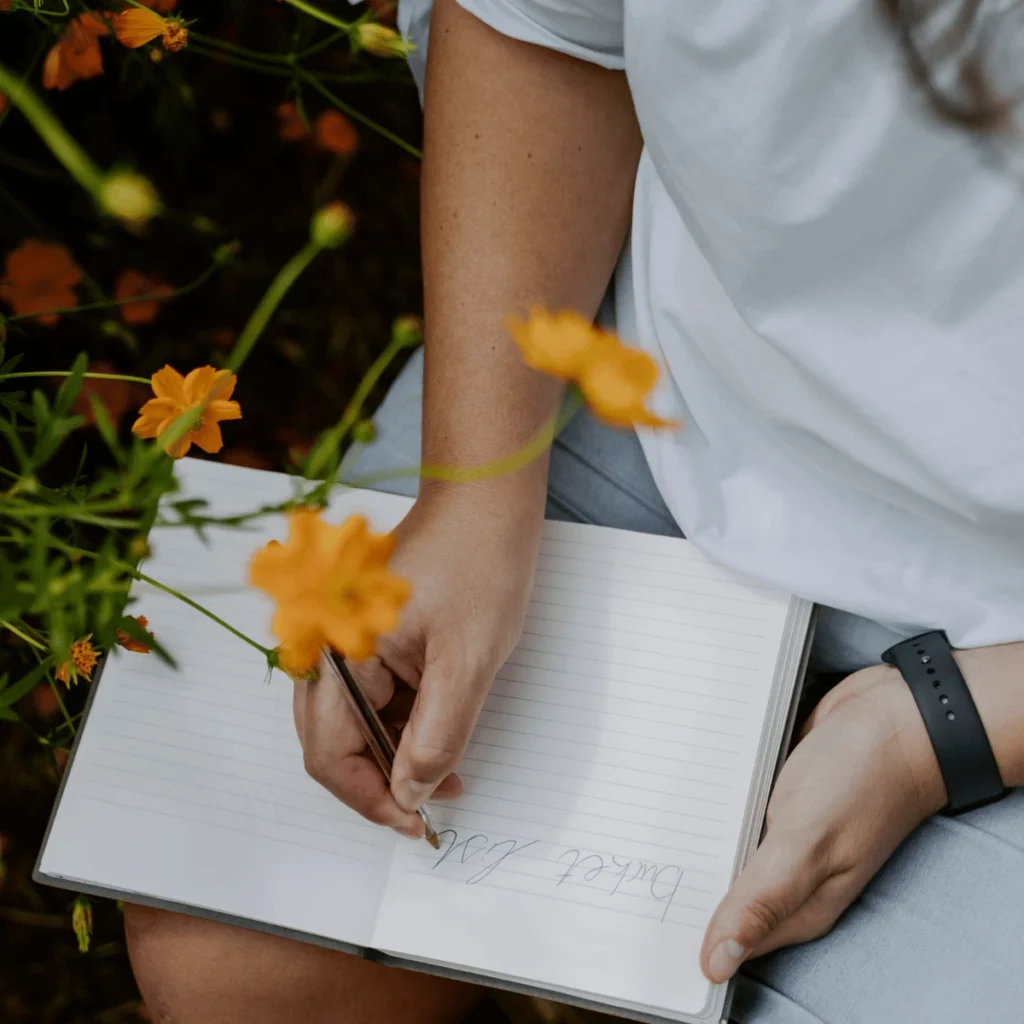 Woman writing in notebook around flowers. powerful manifestation methods