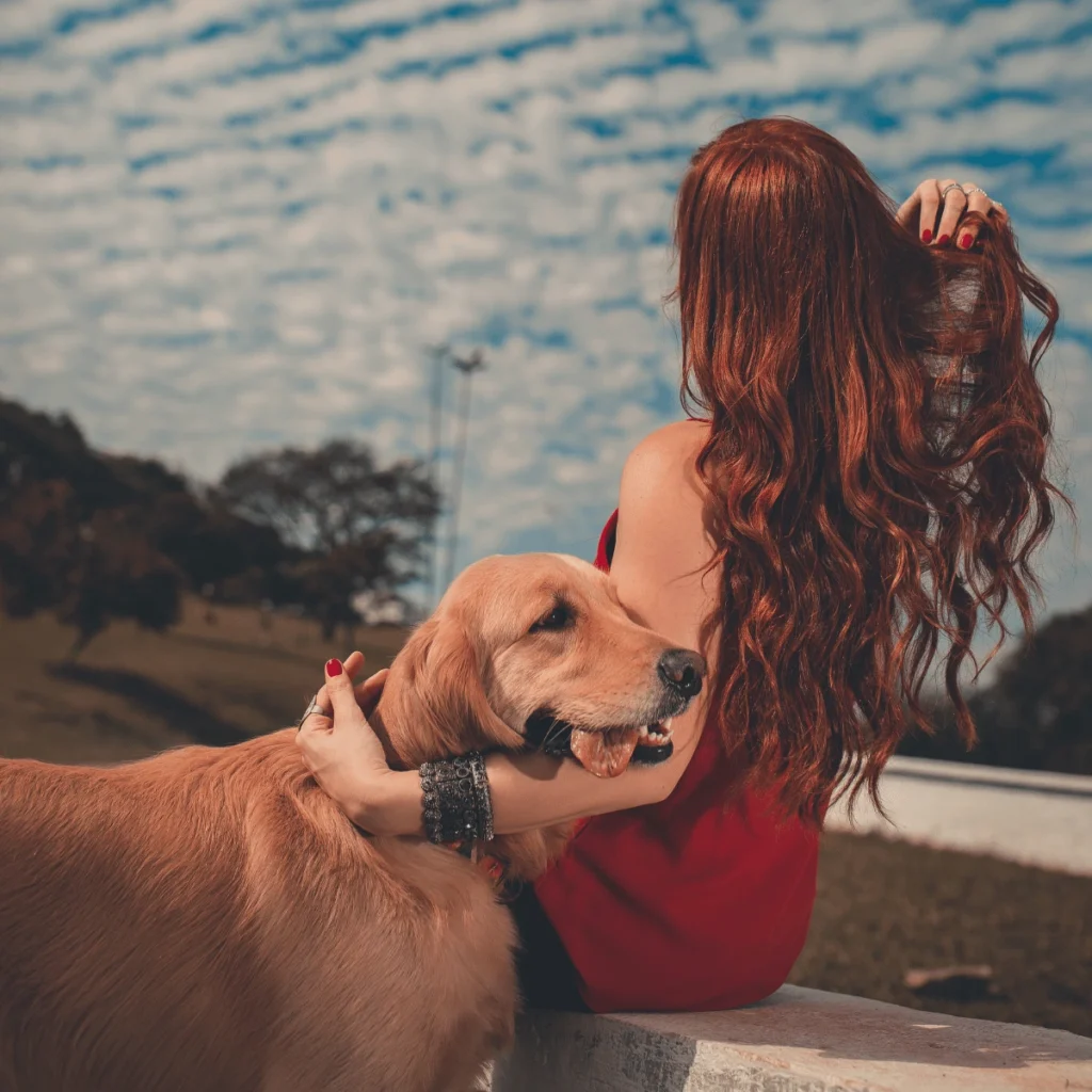 Woman sitting down on a wall with her golden retriever dog next to her