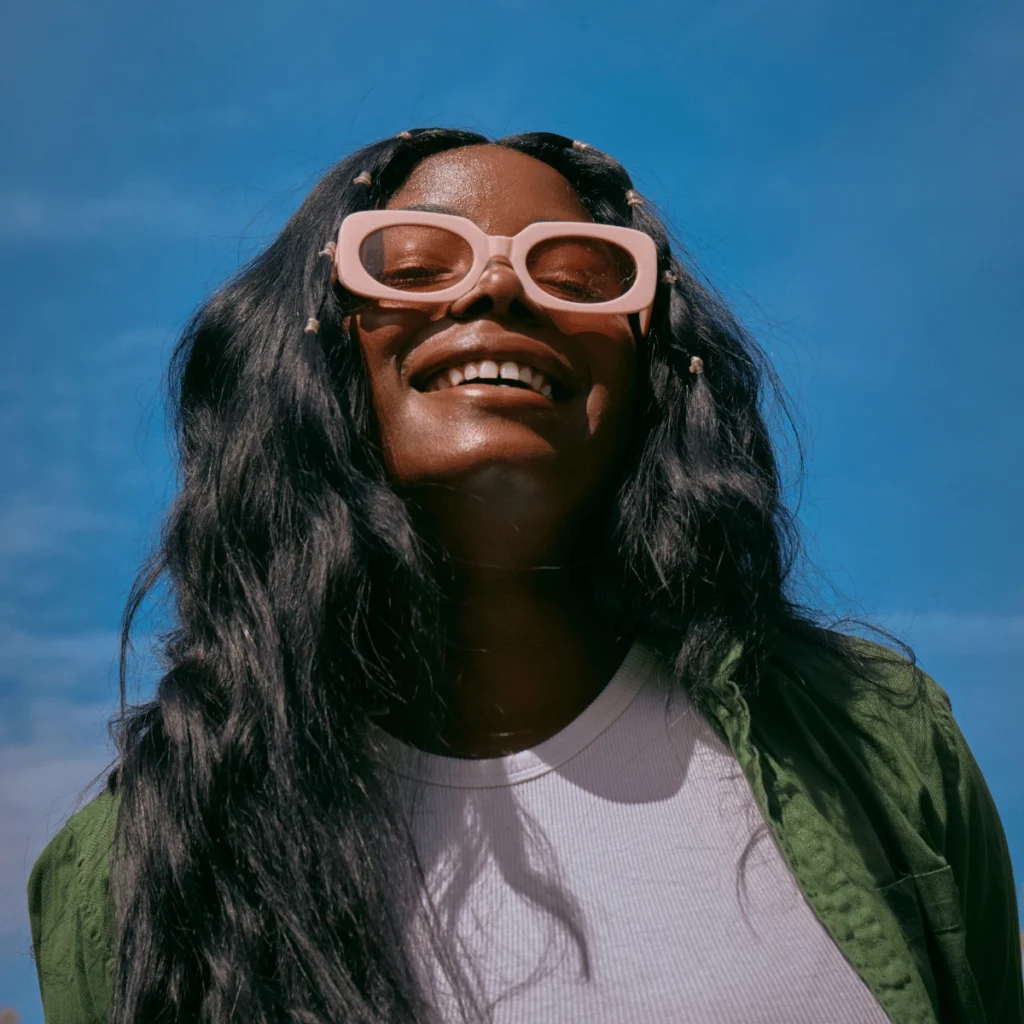 self-compassion journal prompts. woman wearing pink glasses under a summer sky