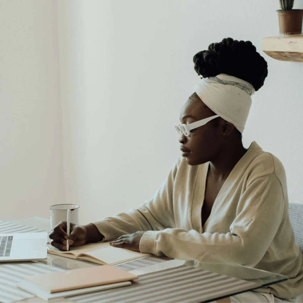 Black woman sitting at a table writing in a notebook