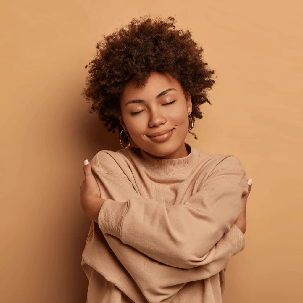 Gentle lovely Afro American woman crosses hands and embraces own body tilts head and closes eyes. Journal Prompts For Self-Care