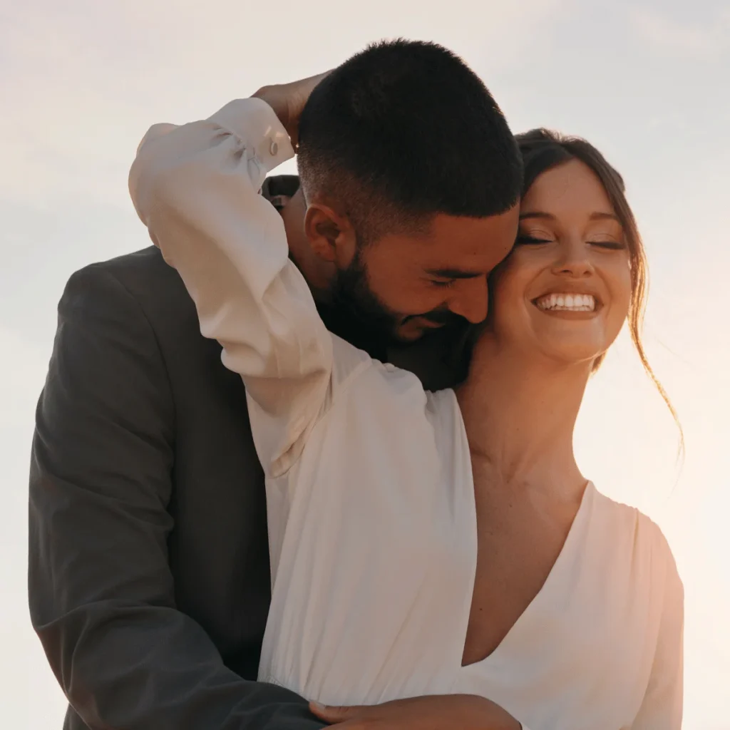 Man hugs a woman from behind who is wearing as white dress. Affirmations To Attract Love