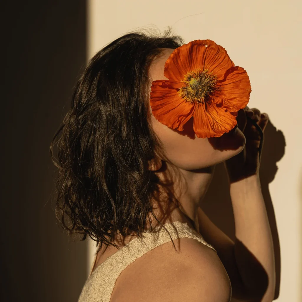 Woman holding a large orange flower to her face in a dimly lit room. Affirmations To Attract Love