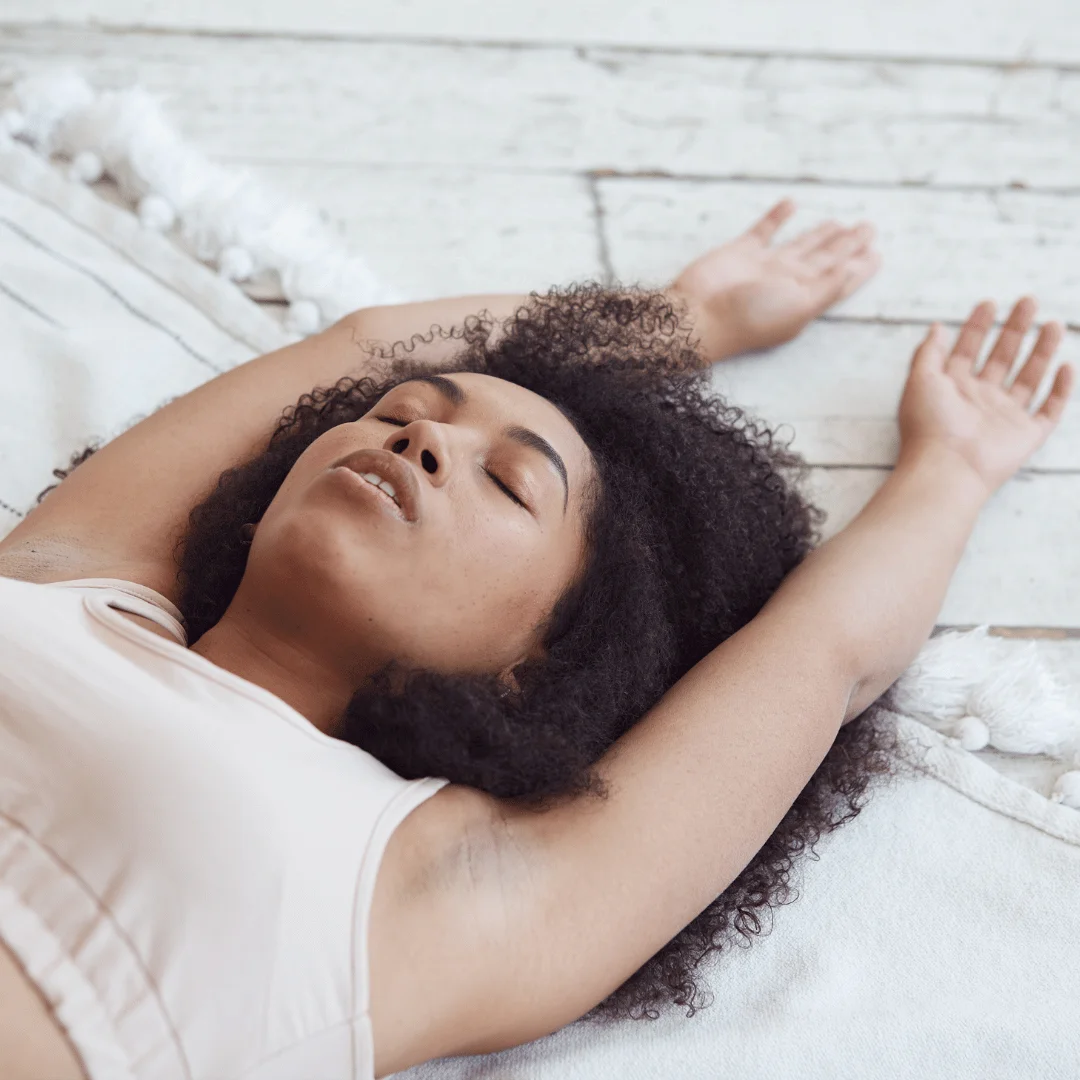 Woman with curly hair laying down with her hands stretched.Somatic Breathing