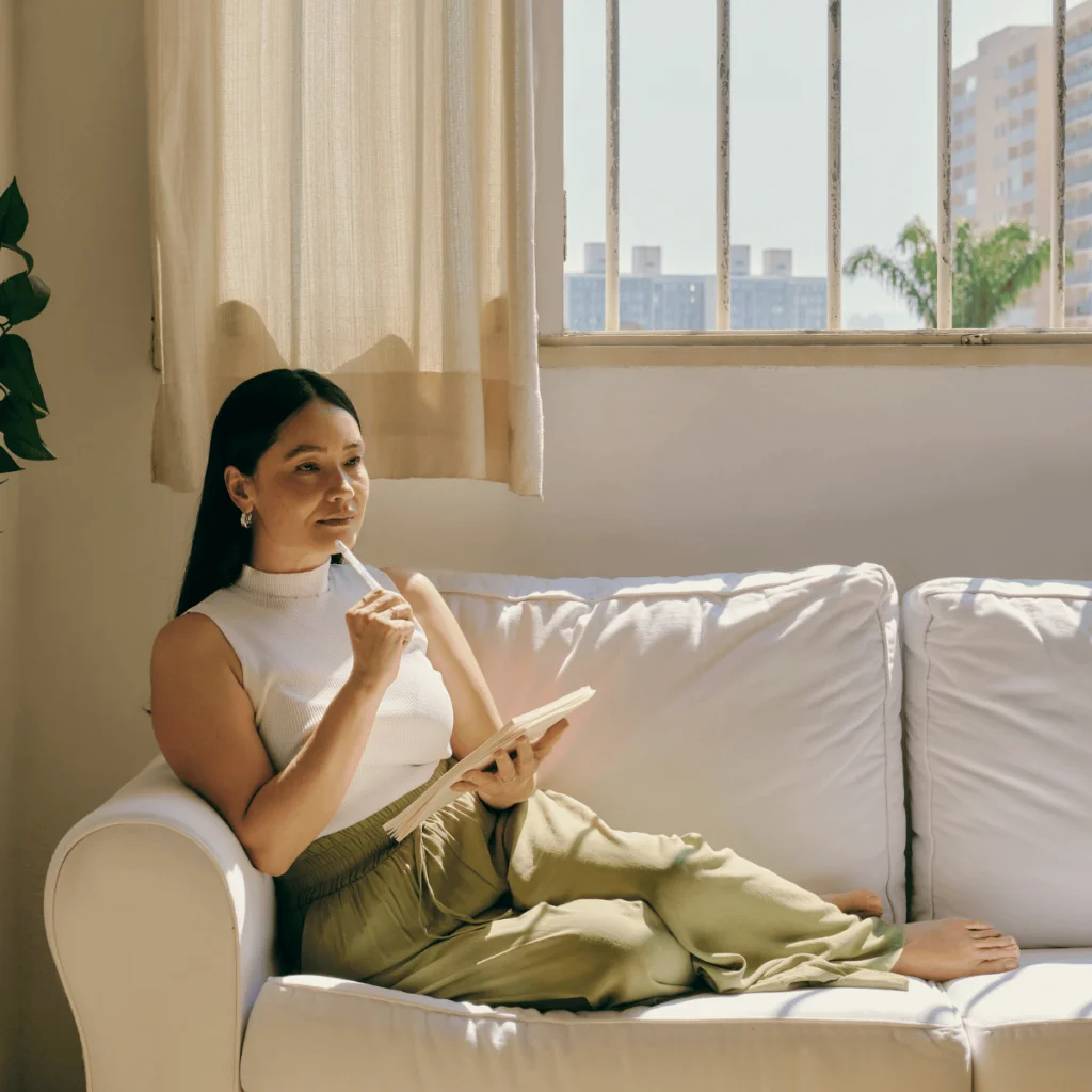 Woman-sits-on-her-cream-coloured-sofa-writing-in-her-journal. Wounded Feminine Energy 